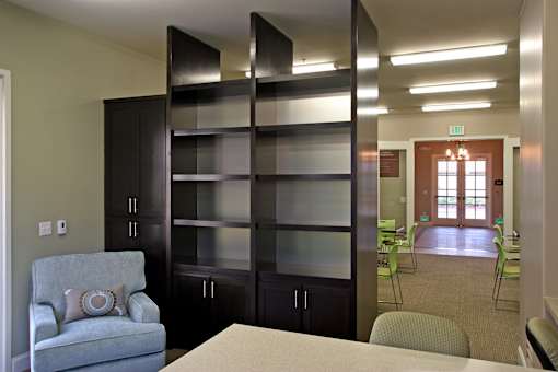 A room with a grey chair and a glass cabinet.