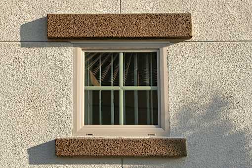 A window with a brown frame is on a light-colored wall.