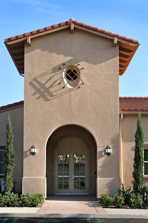 A building with a beige facade and a red tile roof has a large arched doorway.