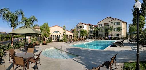A pool surrounded by chairs and umbrellas with a building in the background.