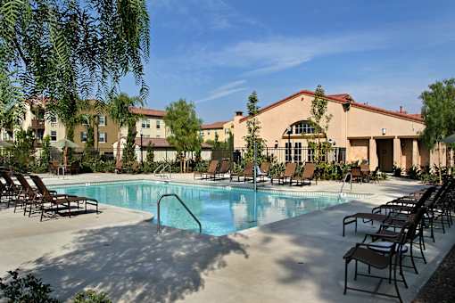 A pool surrounded by chairs and a building in the background.