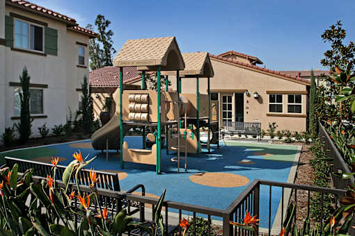 A playground with a slide and swings in front of a house.