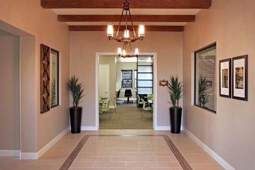 A hallway with a chandelier, potted plants, and framed pictures on the wall.