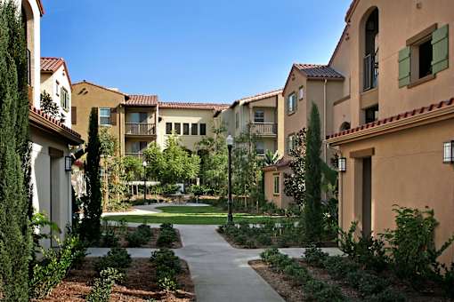 A pathway leads through a landscaped courtyard between two rows of apartment buildings.