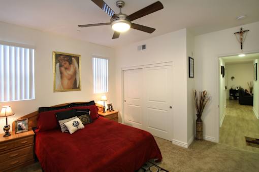 A bedroom with a red bedspread and a ceiling fan.