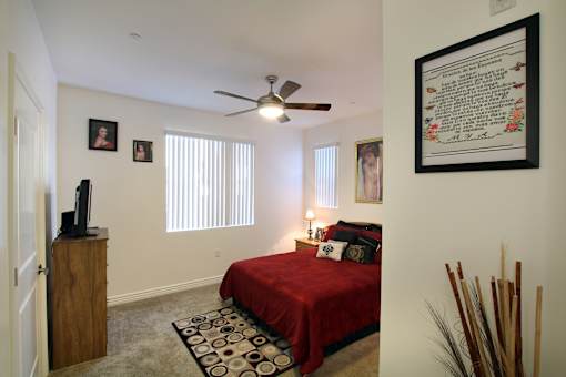 A bedroom with a red bedspread and a ceiling fan.