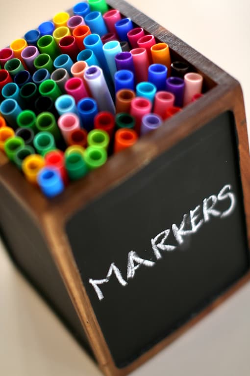 A box of colorful markers with a blackboard that says "markers".