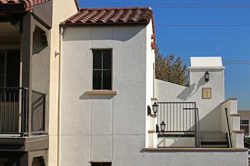 A white house with a red tile roof and a black metal railing.