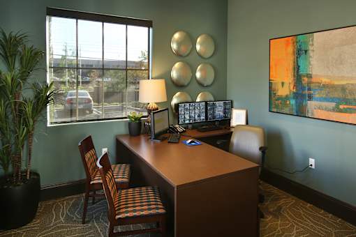 A room with a desk, chairs, and a painting on the wall.