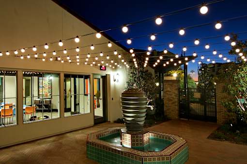 A patio with a pool and lights strung above it.