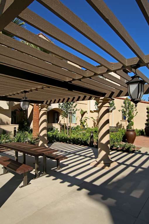 A patio with a bench and a lamp post under a wooden pergola.