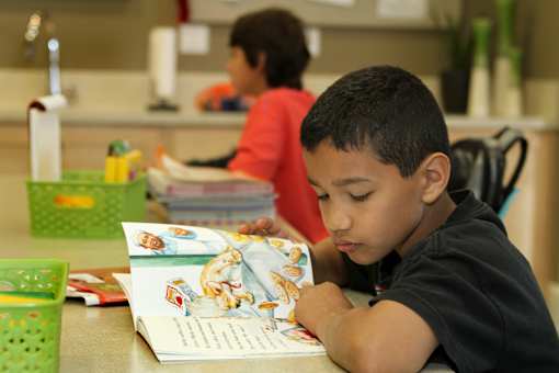 A young boy is reading a book in a classroom setting.