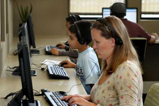 A woman and a boy are using computers in a room with other people.