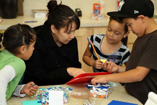 A woman and two children are working on a craft project together.