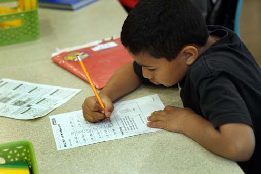 A young boy is writing on a piece of paper with a pencil.