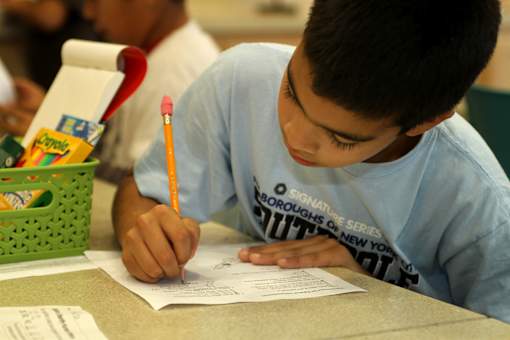 A boy is writing on a piece of paper with a pencil.