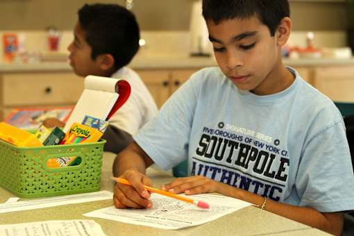 A boy in a Southpole Authentic t-shirt is writing at a table.