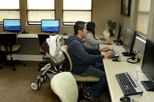 A man and woman are working on computers in an office with a baby in a stroller.