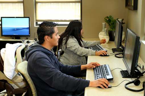 Two people are working on computers in an office setting.