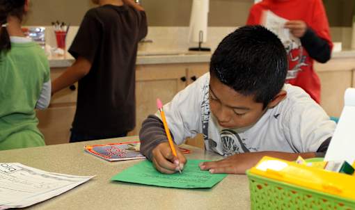 A boy is writing on a green piece of paper.