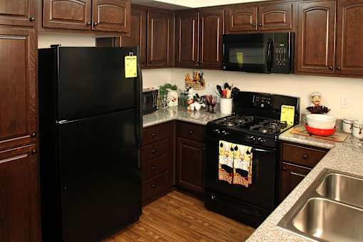 A black refrigerator stands in a kitchen with wooden cabinets and a black stove.