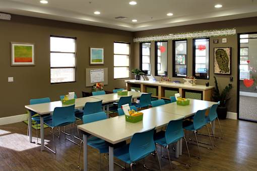 A room with tables and chairs and a long table with a bunch of flowers on it.
