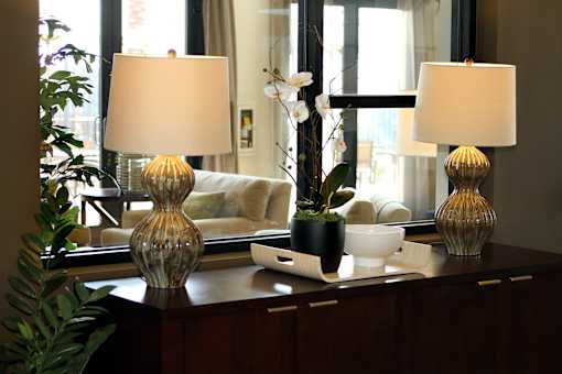 Two table lamps with white shades on a table with a vase and a plant.