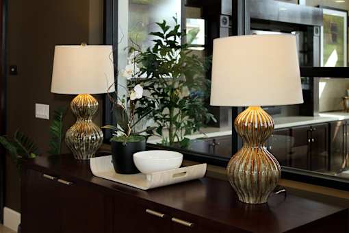 Two table lamps with white shades and two glass vases on a wooden table.
