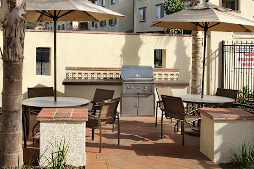 A patio with a grill and chairs under umbrellas.