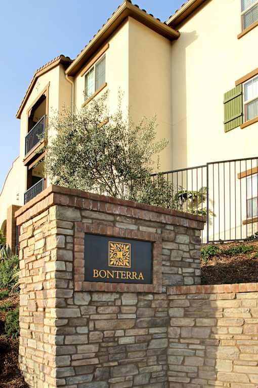 A stone wall with a sign that says Bonterra in front of a tan building.