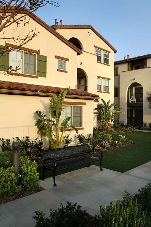 A bench is in front of a house with a green lawn.