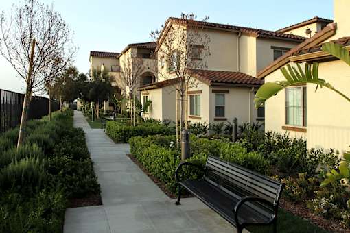 A black bench sits on a sidewalk in front of a house.