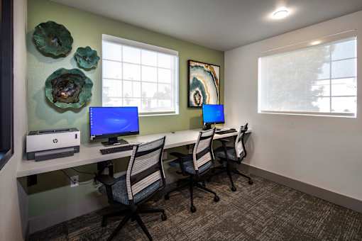 A room with a desk, chairs, and two monitors.