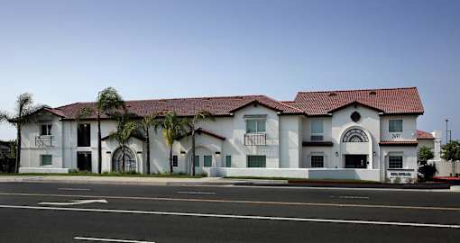A white building with a red roof and palm trees in front.