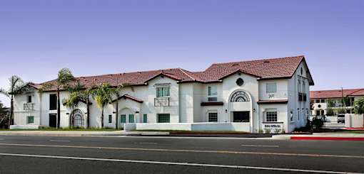 A white building with a red roof and palm trees in front.