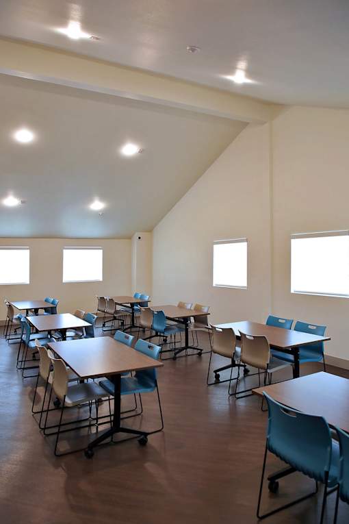 A classroom with tables and chairs and windows on the wall.
