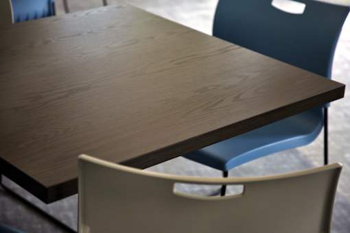 A brown table with a blue chair and a beige chair in front of it.