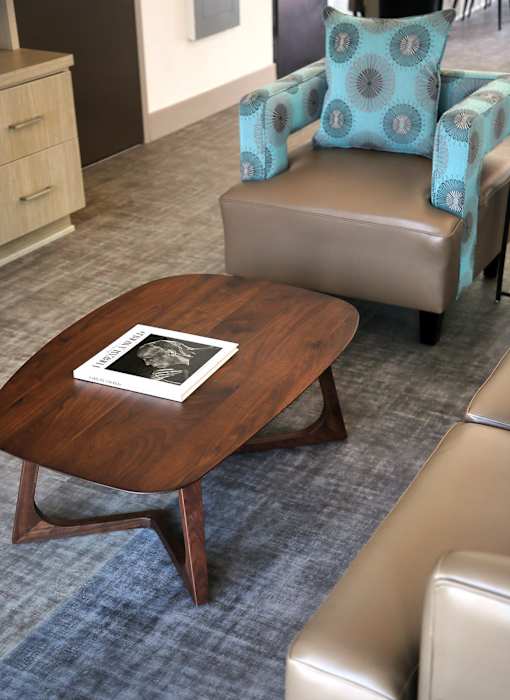A brown coffee table with a book on it sits in front of a blue chair.