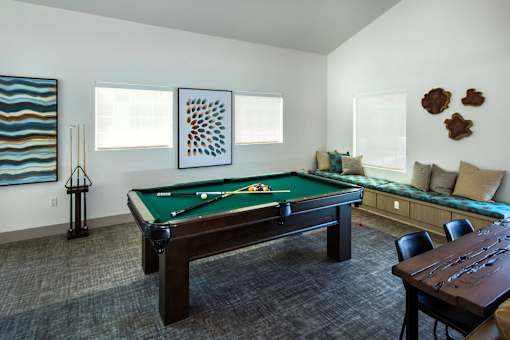 A pool table is in the middle of a room with a brown table and chairs.