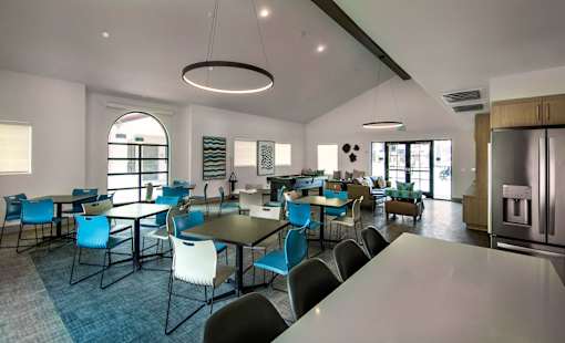 A modern dining room with blue chairs and a kitchen in the background.