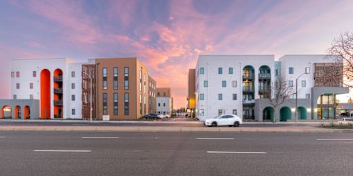 A white car is parked in front of a white building with a red arch.