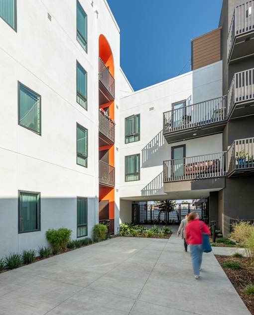 A woman walks down a concrete walkway between two buildings.