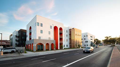 A white building with red arches is situated on a street with cars.