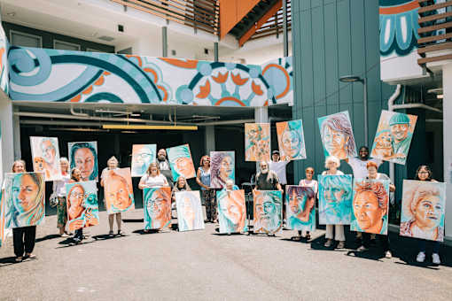 A group of people holding up paintings of women's faces.