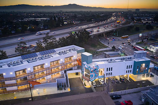 A sunset view of a busy city street with a building that has a sign that reads "SUSTAIN".