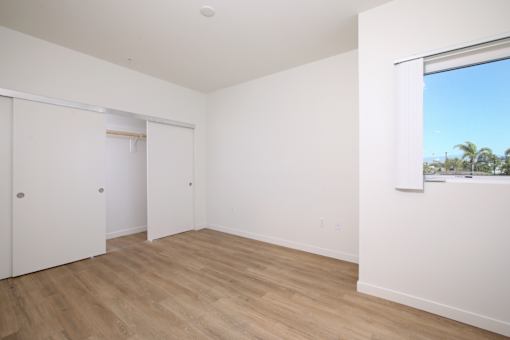 A room with white walls and wooden flooring with a window.