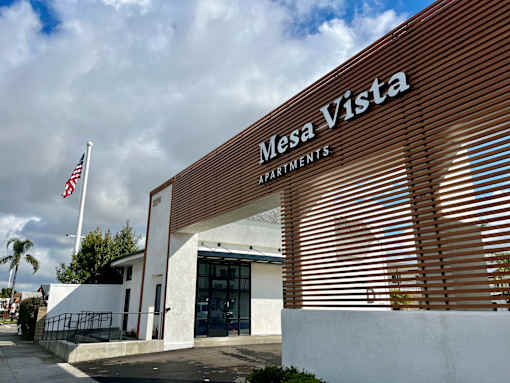 The front of the Mesa Vista Apartments building with a flag flying in the background.