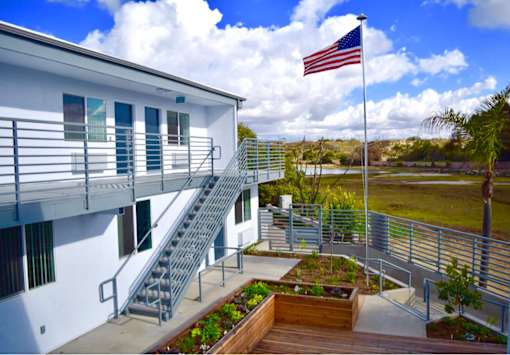 A white building with a flag on top and a staircase leading to the second floor.