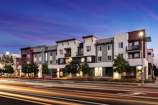 A modern apartment building with a lit up street in front.