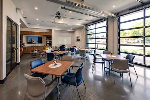 A conference room with a long table and chairs, a television on the wall, and a view of the outdoors through large windows.